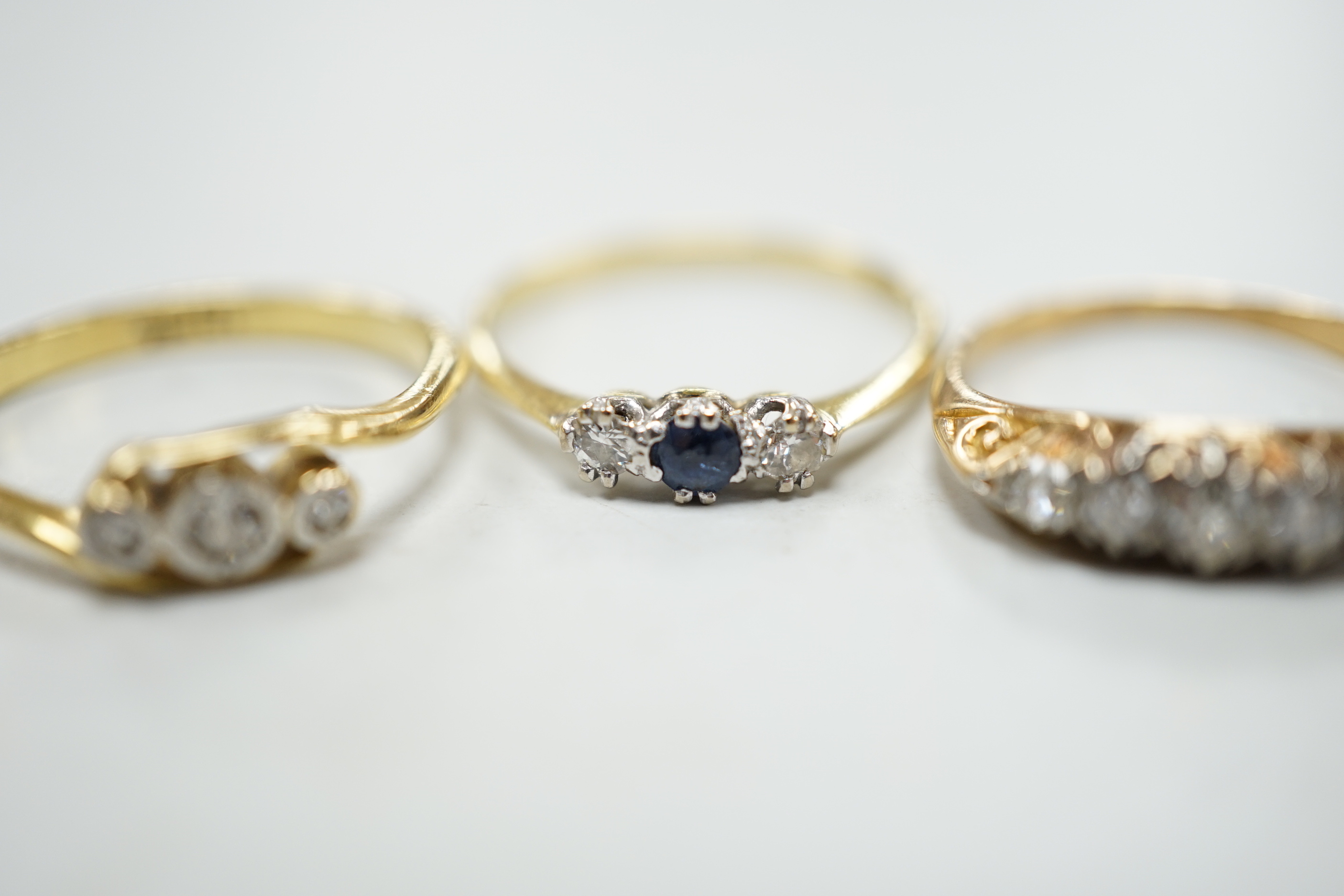 Two 18ct rings including illusion set three stone diamond and sapphire and diamond three stone and a yellow metal and graduated five stone diamond set half hoop ring, gross weight 5.8 grams.